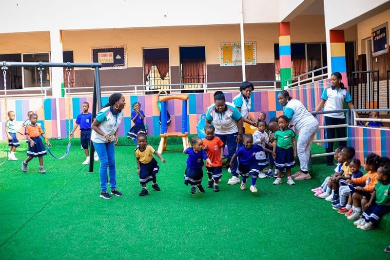 Nursery children playing a group game with their teachers on the B and B School playground